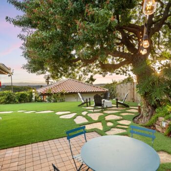 a small backyard with a blue table, chairs and a large tree